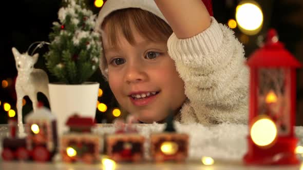 Little Girl Sprinkles Snow on Christmas Tree on Background of Garland Lights