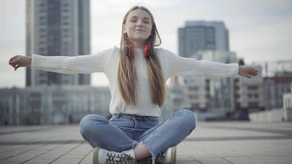Relaxed Caucasian Woman Sitting in Lotus Pose on Overcast City Square. Portrait of Calm Smiling alt