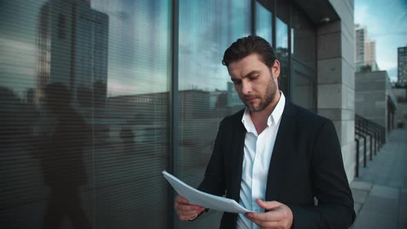 Businessman with Documents Walking Near City Building. Man Reading Documents alt