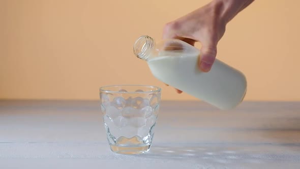 Male Hand Pouring Milk In Glass On White Table