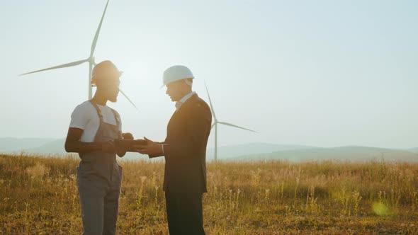 Coworkers Examining Wind Turbines Using Modern Tablet Outdoors alt
