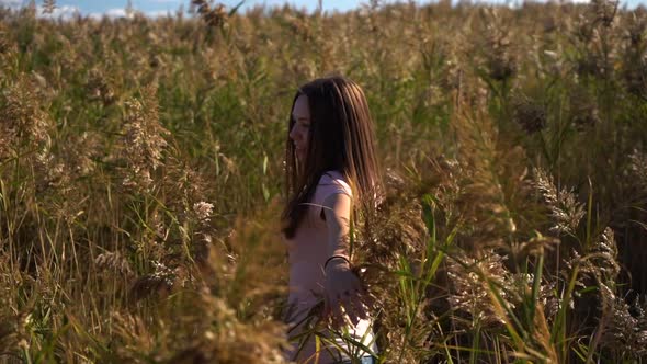 Young Woman or Girl in Pink T-shirt and Blue Jeans Spinning in Slow Motion in Field of Reed or Cane alt