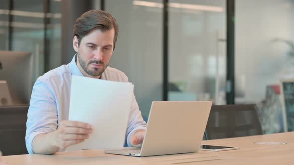 Mature Adult Man with Laptop Reading Documents in Office alt