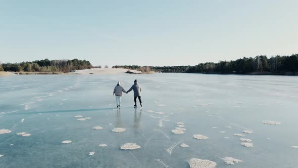 Aerial Shot of Couple Skating on a Blue Frozen Lake in Beautiful Sunny Landscape