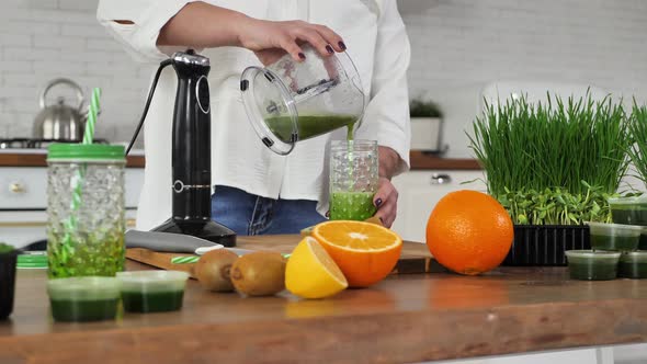 Young Woman Pours a Fruit and Vegetable Cocktail with Witgrass Into a Jar with a Straw