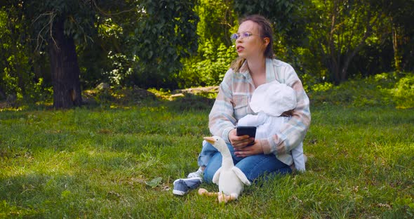 Young Mother with a Child During a Walk Outdoors Mom Watches a Video Through an Online Application alt