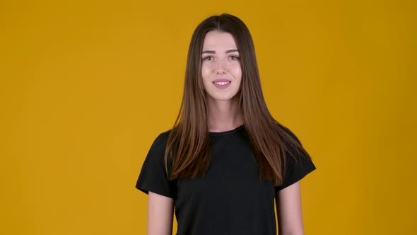 Positive young girl smiling and looking at the camera isolated on yellow background.
