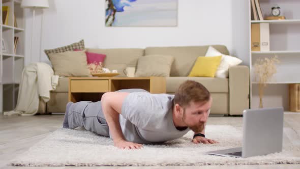 Man Doing Push Ups and Watching Workout Video on Laptop alt