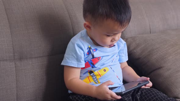 Little Boy Playing Smartphone On Sofa alt