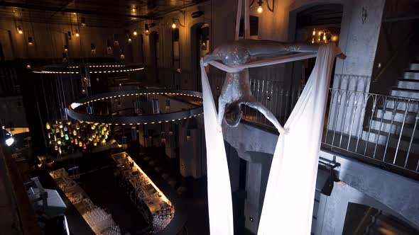 Female aerialist doing the upside down straddle pose in a music club. alt