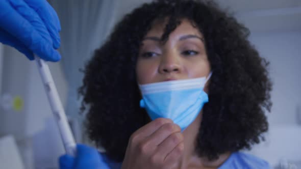 Female mixed race patient wearing protective clothes having covid swab test alt