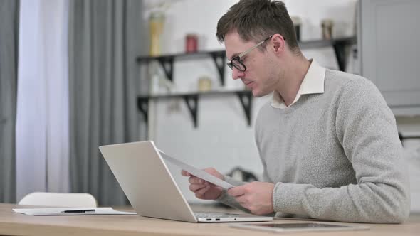 Young Man Using Laptop for Paperwork alt