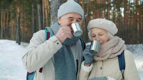 Happy Family Senior Man and Woman Clanging Metal Cups and Drinking Outdoors in Winter Wood alt