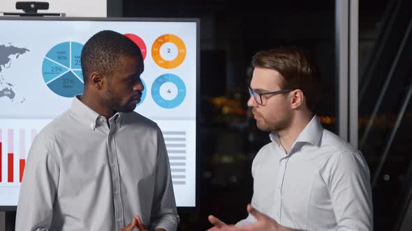 Two analysts of different ethnicity discussing business strategy in the office late alt