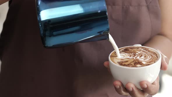 Barista pouring steamed milk in coffee cup making Latte art