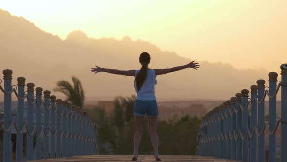 Happy Woman Jumping Up Outdoors on Wooden Deck Enjoying Warm Tropic Evening alt