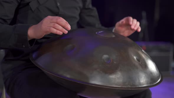 Close up view of musician hands playing handpan drum on big concert hall stage alt