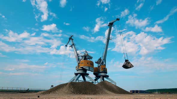 Two Port Cranes Work with Crushed Stones, Moving Them in Piles alt