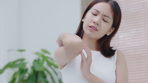 Young Asian woman scratching her elbow because of dry skin problem. alt