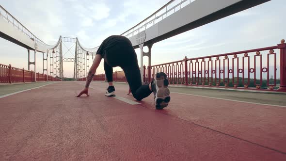 Young Man in Black Sports Uniform Runs on the Pedestrian Bridge at Dawn alt