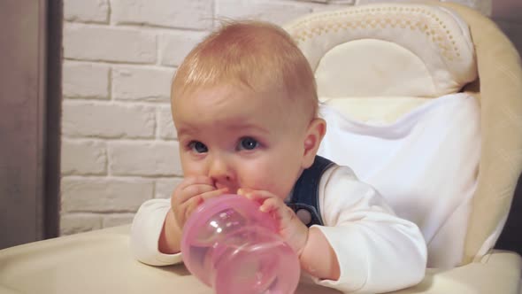 Baby Holding Bottle of Water in His Hands Looks at Camera and Smiles