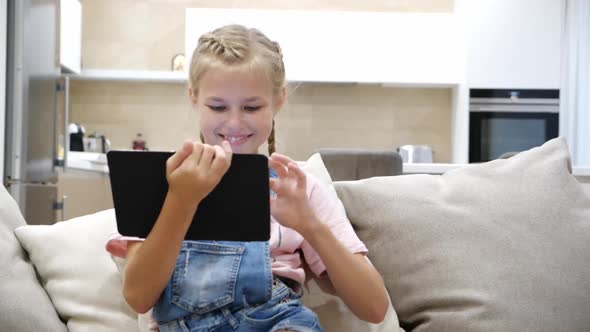 Preteen Child Playing Tablet and Listening to Music While Relaxing on Couch in Living Room at Home