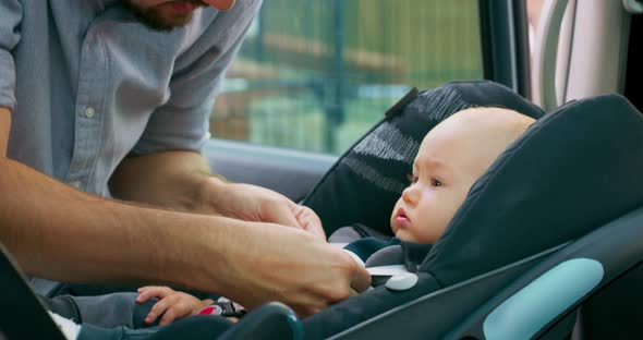 Camera Inside the Car Closeup Baby Boy Sits in the Baby Car Seat Inside of Car Young Bearded Father alt