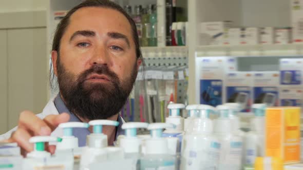 Bearded Pharmacist Smiling To the Camera, While Working at Drugstore alt
