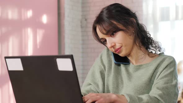 Girl Sitting at Laptop in Her Living Room Talking on Phone and Writing Notes alt