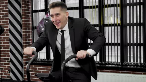 Businessman in a Black Suit is Engaged on an Exercise Bike in a Boxing Club