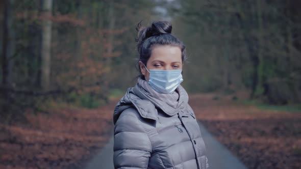Woman in Forest Turns Around Removes the Protective Mask From Face and Smiles alt