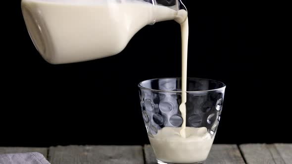 Person pours fermented baked milk from a jug into a glass. alt
