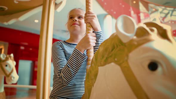 Happy European Blond Teen Smiling While Riding a White Carousel Horse alt