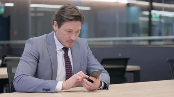 Middle Aged Businessman using Smartphone in Office  alt