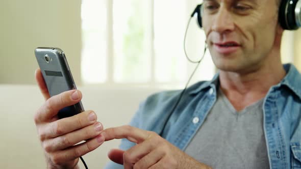 Man listening music on mobile in living room alt