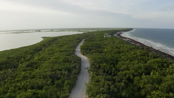 Aerial shot of a Car driving along a beautiful road between two beaches in Mexico. alt