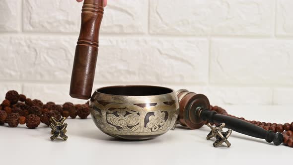 hand rotates a wooden stick around a copper singing bowl alt