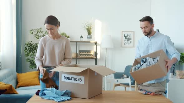 Man and Woman Packing Clothes in Donation Box at Home When Child Bringing Teddy Bear Sharing Toy alt