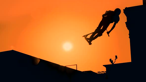Slow Motion: Teenager Silhouette Showing High Jump Tricks on Scooter at Sunset