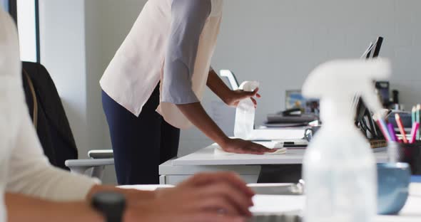 African american businesswoman wearing face mask, sanitizing desk in office alt