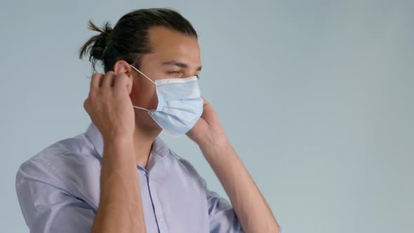 Close up of brunette man putting on hygienic mask. Static, bluish background alt