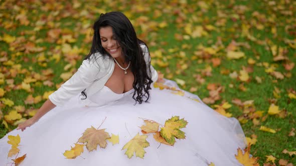 Happy Bride in Autumn Beautiful Busty Woman in White Dress is Sitting on Lawn alt