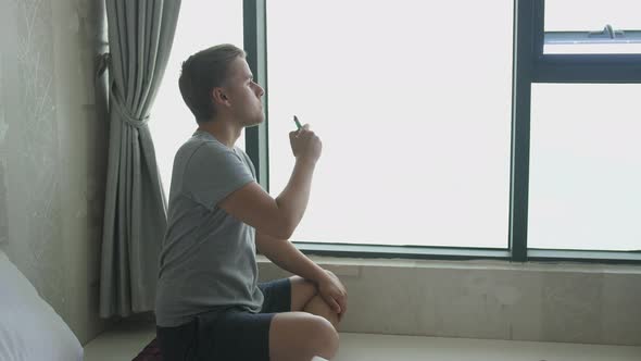 Man Smoking Electronic Cigarette Pipe By the Window at Home