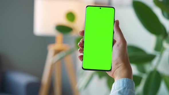 Woman at Home Using Smartphone with Green Mockup Screen in Vertical Mode alt