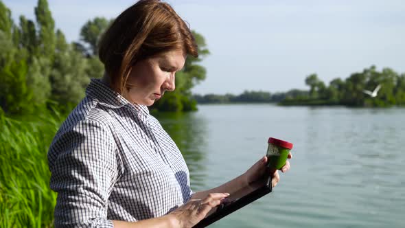 Woman Ecologist Examining Sample of Green Algae and Entering Data on Tablet alt