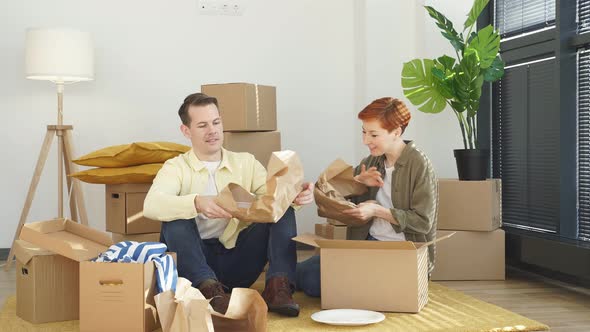 Delighted Woman and Husband Unpack Cardboard Boxes with New Tableware Carry Plates Move Into New