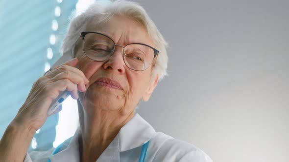 Cheerful senior doctor with eyeglasses talks on mobile phone alt