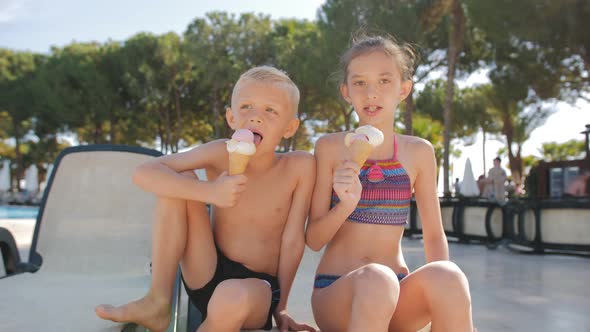 Tenyearold Children a Boy and a Girl Together on a Chaise Longue By the Pool Eating Ice Cream in a