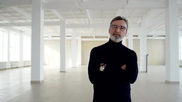 Successful Businessman Stands in Middle of Rented Office Space and Takes Off Glasses Front View alt