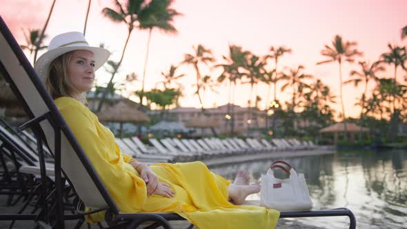 Young Sexy Stylish Woman in Hat and Yellow Dress Relaxing Scenic Swimming Pool alt